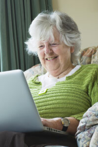 Iloinen ikääntynyt naishenkilö lukee tietoa kannettavalta tietokoneelta.
