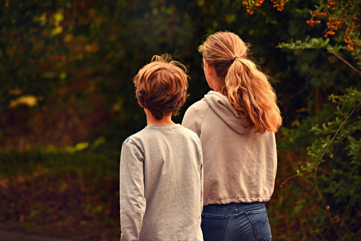 Kuvassa nuori poika ja tyttö kävelevät poispäin metsämaisemassa.