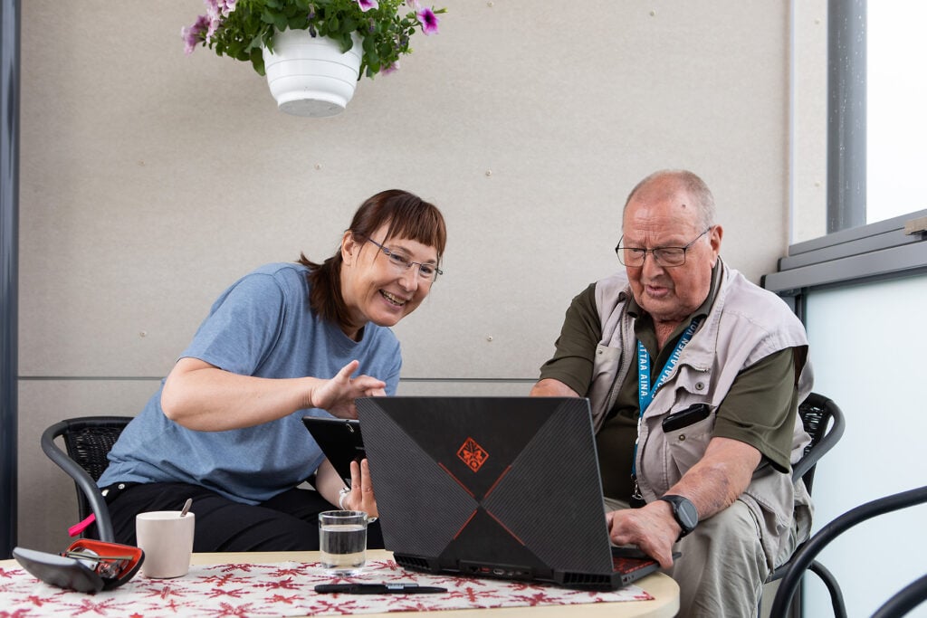 Nainen ohjeistaa ikäihmistä tietokoneen käytössä