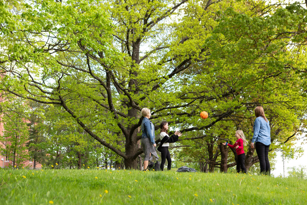 Aikuiset ja lapset heittelemässä palloa puistossa