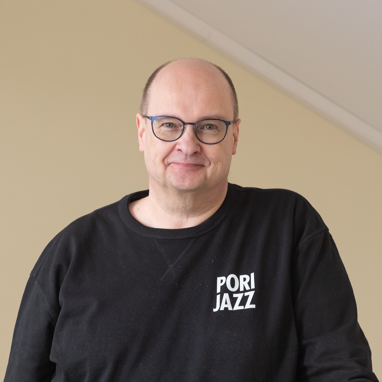 Kuvassa mies, jolla silmälasit ja musta collgepaita, jossa oikealla Pori Jazz -logopainatus.