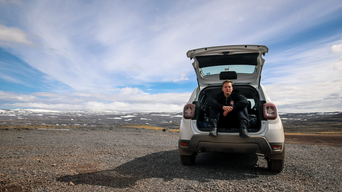 Dimitri istuu autossa ja katsoo kameraan - kaunis maisema näkyy taustalla