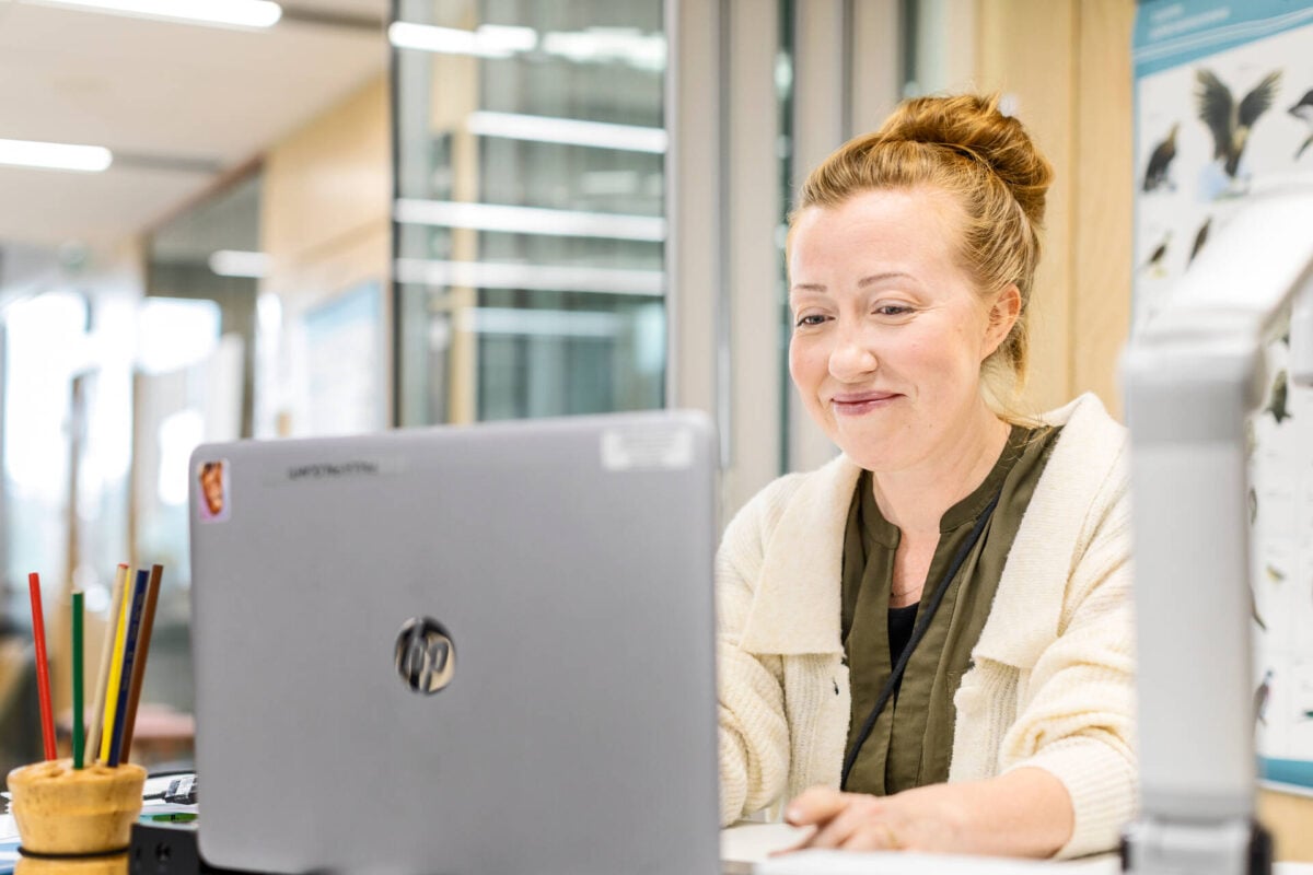 Hymyilevä nainen työskentelee tietokoneella.