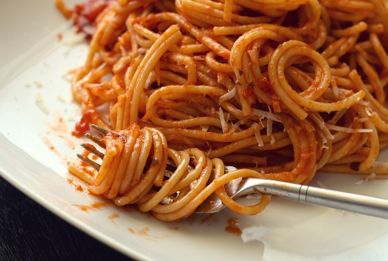 Spagettia ja tomaattikastiketta lautasalla, jossa haarukkaan kääritty spagettia