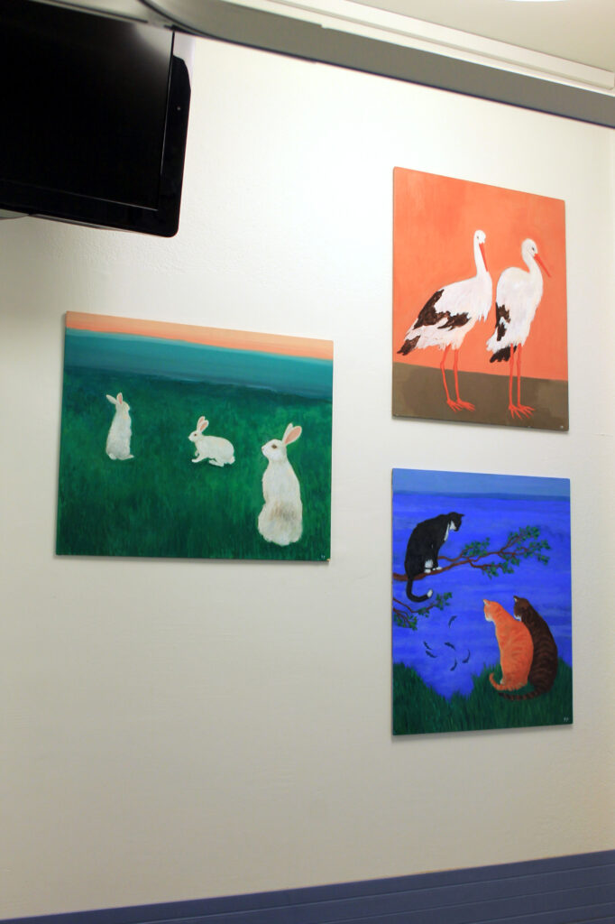 Kuvassa kolme yksittäismaalausta, joissa yhdessä valkoisia jäniksiä vihreäassa maastossa, toisessa kaksi haikaraa oranssitaustaisessa maalauksessa ja kolmannessa sinisävyisessä maalauksessa on kolme kissaa. 