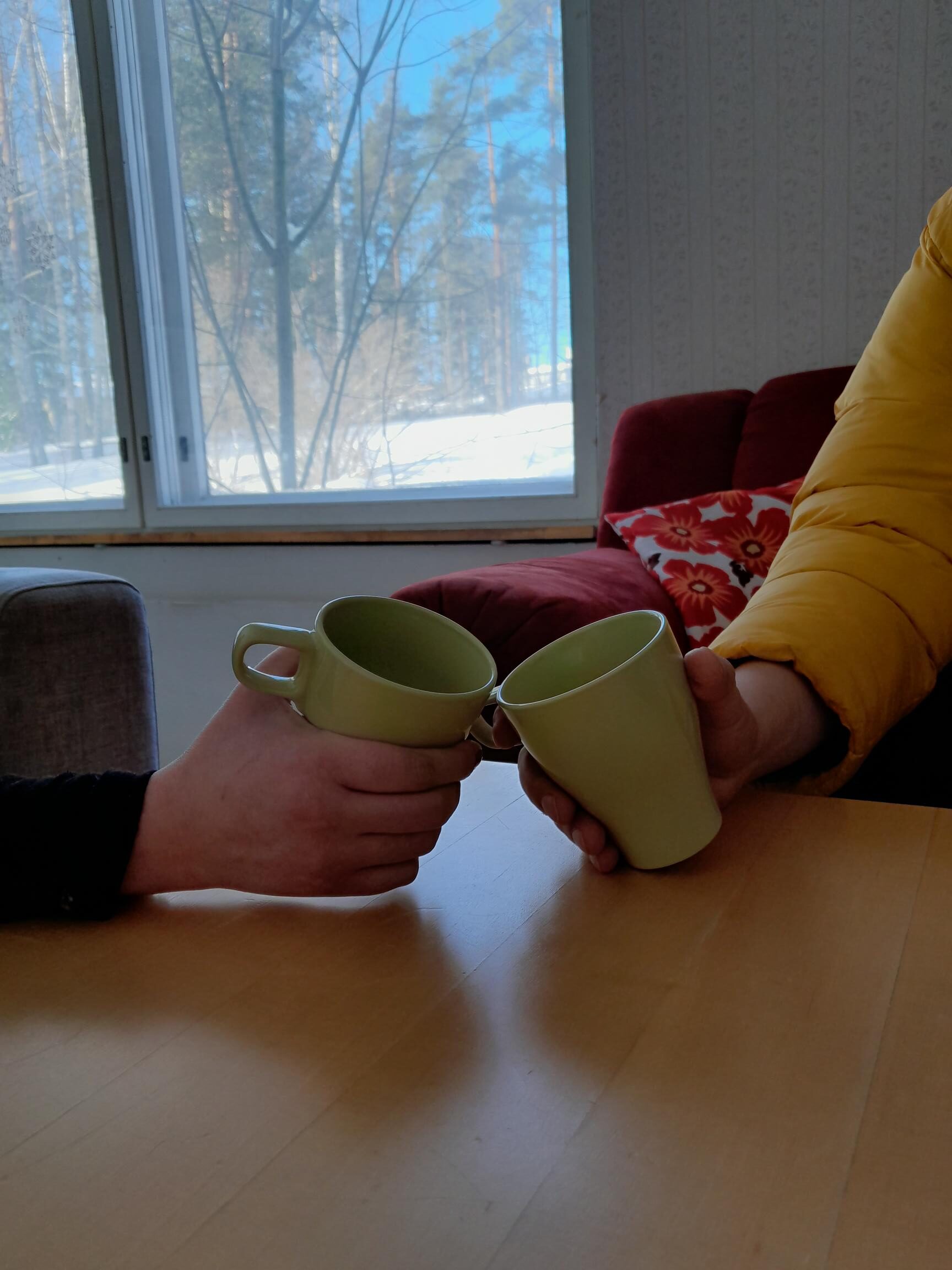 Kuvassa kaksi henkilöä kahvikupit kädessä pöydän ääressä. Kuvassa näkyvät henkilöistä vain kädet.
