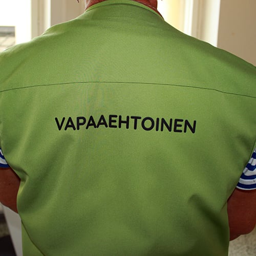 Kuvassa kuvattuna henkilö takaapäin niin, että hänestä näkyy vain selkämys, jossa vihreässä vaatetuksessa teksti vapaaehtoinen.