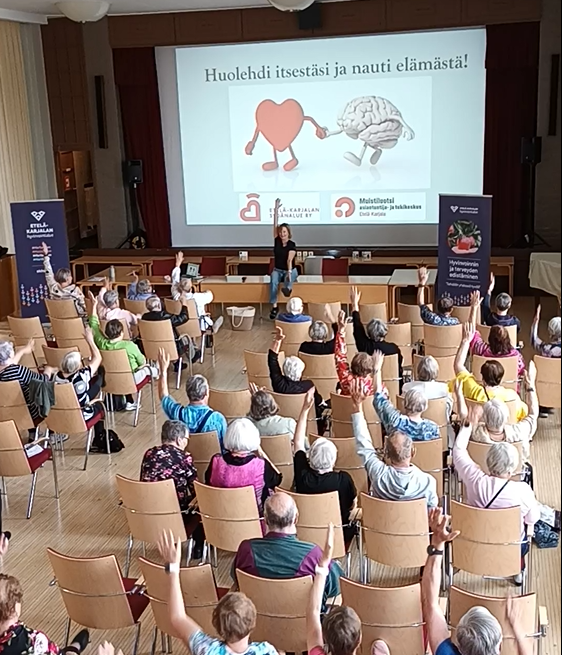 Salillinen ikäihmisiä taukojumppaa tuolilla istuen