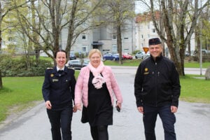 Kolme ihmistä kävelee hymyillen kuvaajaa kohti, keskimmäisellä on vaaleanpunainen takki ja reunimmaisilla on pelastuslaitoksen virka-asut päällä.