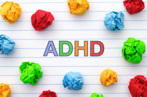 Kuvassa on teksti ADHD ja erivärisiä rytistettyjä paperipalloja vaalealla taustalla.