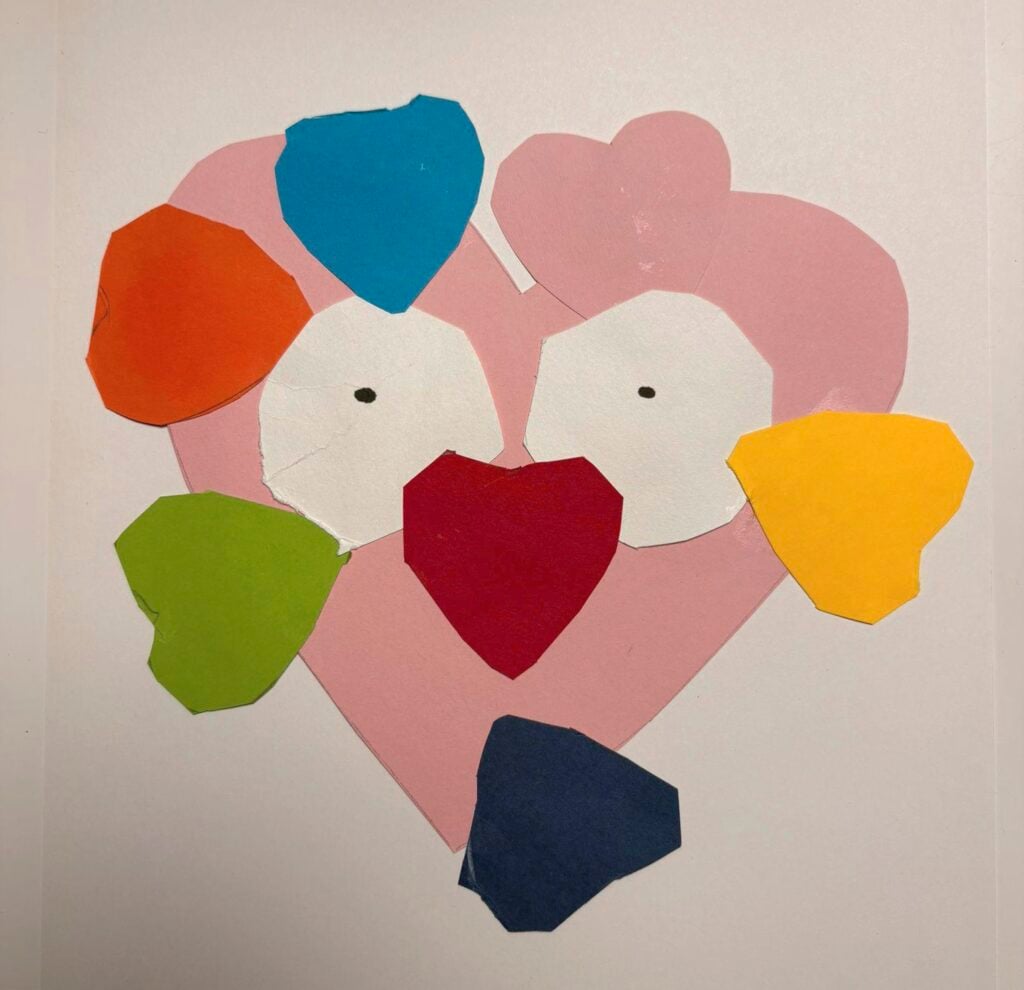 Värikäs lapsen tekemä askartelu, jossa on sydämen muotoinen vaaleanpunainen pää, jolla on silmät ja punainen sydännenä