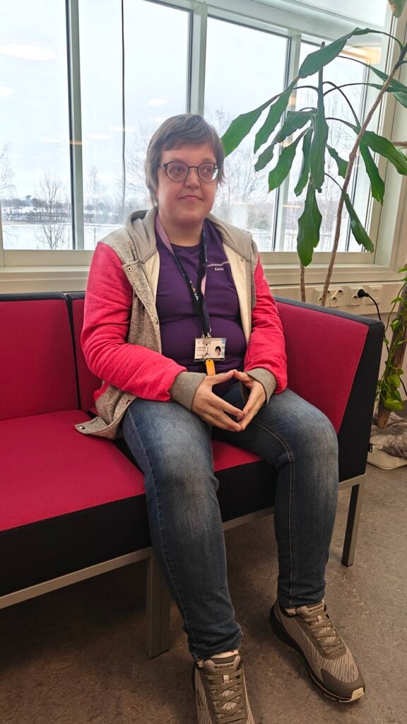 Nainen istuu sohvalla ja katsoo sivuun, takana on järvimaisema