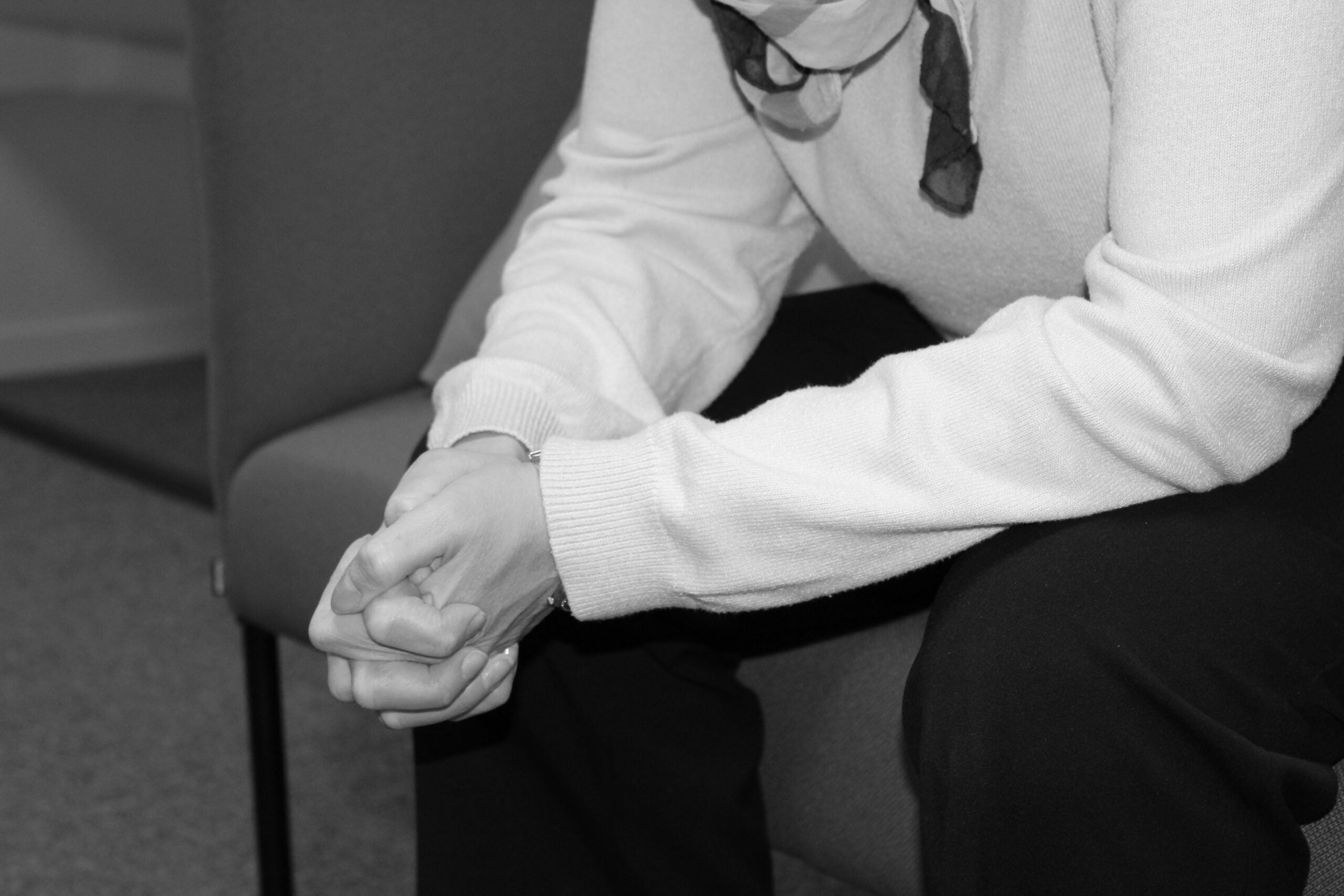 nainen istuu sohvalla ja vääntelee käsiään - kuva on mustavalkoinen