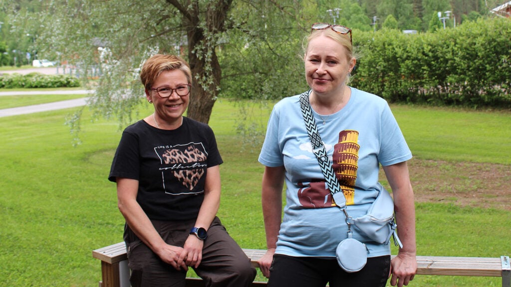 Kaksi naista hymyilevät kesäisen vihreän puutarhan edessä