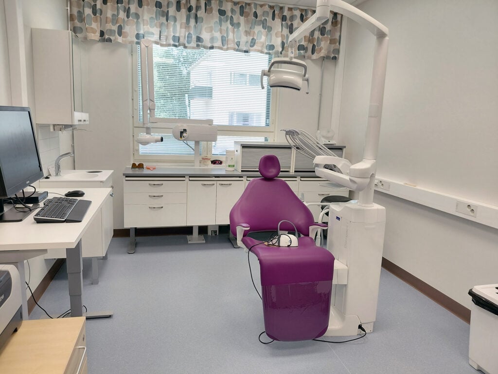 Valokuva hammashoitolan vaaleasta hoitohuoneesta, jossa violetti hoitotuoli.